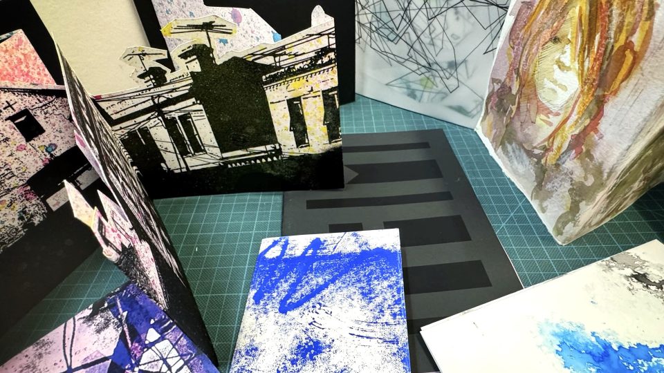 A sample selection of seven handmade artist’s books. Techniques shown with the books include hand-cut designs, monoprinting, watercolour painting and hand drawn pages with subjects including faces, buildings and abstract imagery.